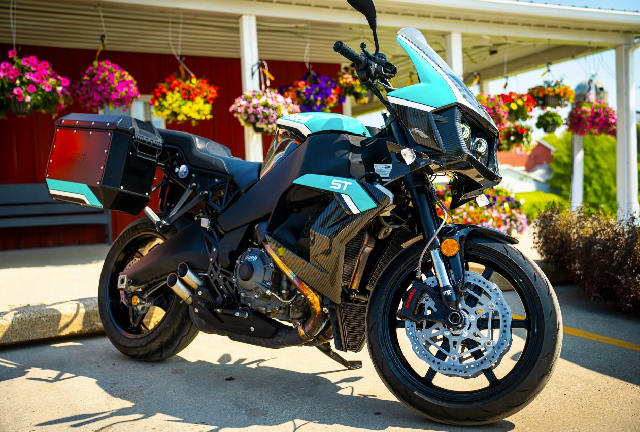 Teal and carbon Buell Super Tourer with hard luggage parked beside hanging flower baskets